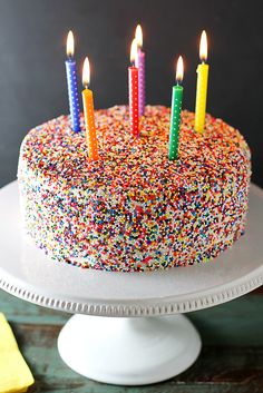 a birthday cake with multi - colored sprinkles and lit candles on top