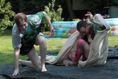 three people on a black tarp in the grass and one person is jumping up