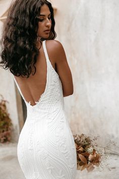 a woman in a white wedding dress with her back to the camera and flowers behind her