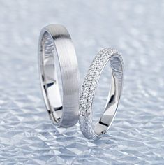 two white gold wedding bands with diamonds on them, sitting on top of a shiny surface