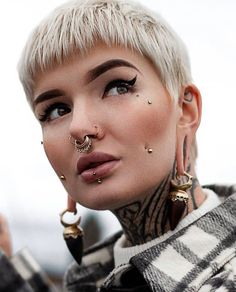 a woman with tattoos and piercings on her face looking at the camera while wearing ear rings