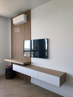 a flat screen tv sitting on top of a wooden shelf next to a wall mounted air conditioner