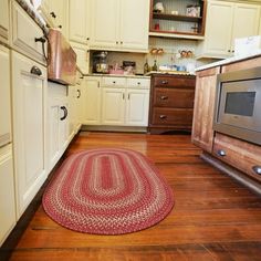 a kitchen with wooden floors and white cupboards has a red rug on the floor