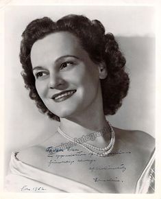 an old black and white photo of a woman with pearls on her neck, smiling at the camera