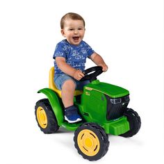 a little boy riding on top of a green toy tractor with yellow wheels and smiling