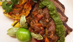 a white plate topped with meat and veggies next to a green pepper wedge