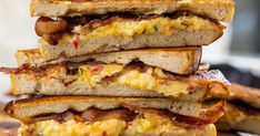 three sandwiches stacked on top of each other with bacon and eggs in between the two halves