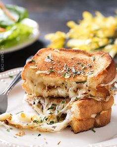 a grilled cheese sandwich on a white plate with a fork and salad in the background