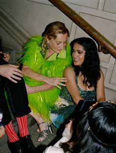 two women dressed in bright green sitting on the stairs and talking to each other while others look on