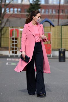 a woman in a pink coat and black pants is walking down the street wearing a face mask