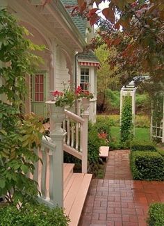 a brick walkway leading to a white house with green trimmings and red flowers