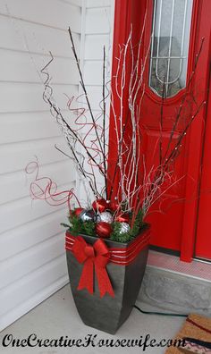 a potted planter with branches and ornaments in front of a red door that says christmas