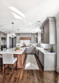 a large kitchen with wooden floors and white counter tops, along with gray cabinetry