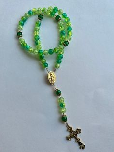 This rosary is made with 8mm shades of green and ombre glass crackle beads. When the sun hits the beads they shine and sparkle so beautifully! This unique rosary features bead caps on each Our Father beads as well as seed beads for separation. The centerpiece and crucifix are gold finished. The total length of the piece is 14 inches long and has been strung onto beading wire and held together with crimp tubes. We take great care while making our rosaries so we are sure they are strong, but if re Green Spiritual Beads For Healing, Green Oval Beaded Jewelry 8mm, Adjustable Green Beaded Necklace With 8mm Beads, Green Faceted Spiritual Beads, Green Faceted Glass Beads, Green Rosary With Round Beads As Gift, Handmade Adjustable Green Rosary Bracelet, Green Handmade Adjustable Rosary Bracelet, Adjustable Handmade Green Rosary Bracelet