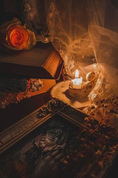 a lit candle sitting on top of a table next to an open book and roses