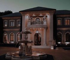 a large house with a fountain in front of it at night time and lights on the windows