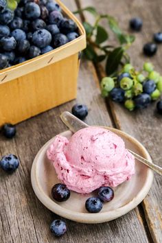 a bowl of ice cream with blueberries on the table next to it and a basket of grapes