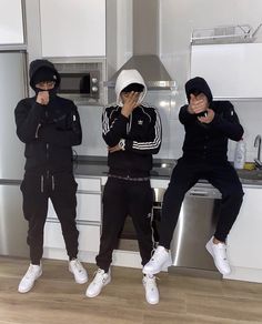 three young men standing in front of a stove top oven wearing black and white outfits