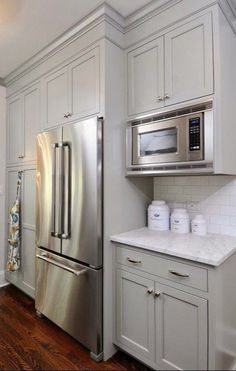 a stainless steel refrigerator and microwave in a white kitchen with wood floors, cabinets and drawers