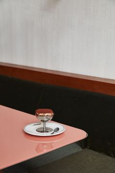 a pink table topped with a dessert on top of a white plate next to a black wall