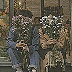 two people sitting on the ground with flowers in their hands