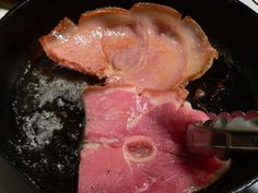 ham being cooked in a skillet with tongs