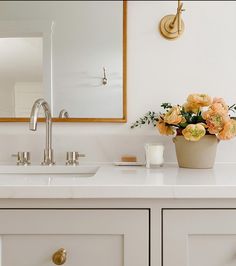 a bathroom sink with flowers in a vase on the counter and a mirror above it