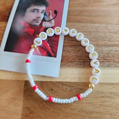 a white beaded bracelet with the words happy birthday written on it and a photo in the background