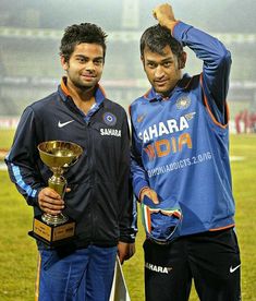 two men standing next to each other on a soccer field holding up their trophy cups