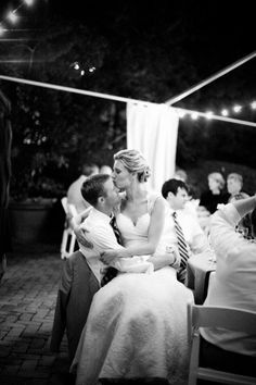 a bride and groom kissing in front of an audience at a wedding reception with string lights on the ceiling