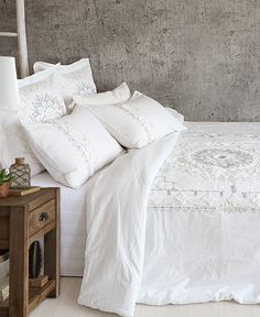 a bed with white linens and pillows on top of it next to a night stand