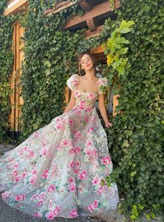 a woman standing in front of a green wall wearing a dress with flowers on it