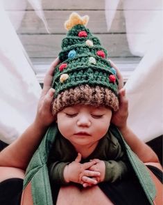 a small child wearing a knitted christmas tree hat