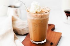 there is a drink with whipped cream in it on a wooden board and some coffee beans