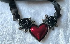 "The black roses and bloody red heart of dispassion, a telltale mark of the female corsair, amorous she wolf and destroyer of men's hearts. A pearlescent-effect trans-red enamelled pewter heart necklace motif, flanked either side with roses with a black acrylic flower and on a split 38\", (96cm) long, doubled, 7mm black ribbon necklace, to be hand tied. The choker comes with a velvet gift pouch. Choker made by Kiss of a red rose with help from Alchemy England 1977." Jewelry Wishlist, She Wolf, Black Roses, Acrylic Flower, Ribbon Necklace, The Heart Of Man, Acrylic Flowers, Black Acrylic, Black Acrylics