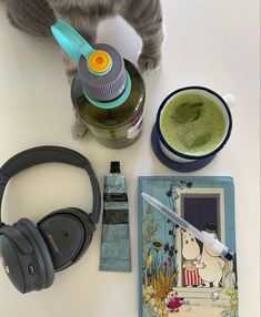 a cat standing on top of a table next to headphones and a bottle of liquid