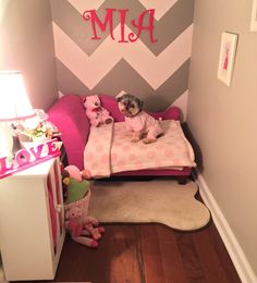 a small child's room with pink and gray walls, chevroned wallpaper and a dog on the bed