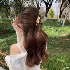 a woman with long brown hair wearing a white shirt and flower clip in her hair