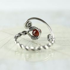 A special silver and garnet ring with a twist and open spiral design. It's adjustable and perfect as a gift if you're not quite sure of the size you need. The shank is twisted from one wire and in the loop at the end is nestled an AA-plus faceted wine red garnet bead and the opposite ends are shaped into spirals. Both twists and spirals are classic and has been used since Celtic times in jewellery. I think my Danish heritage is shining through. :o) Garnet is a stone of positive thoughts which is Handmade Adjustable Ruby Ring, Adjustable Red Spiral Jewelry, Handmade Adjustable Silver Ruby Ring, Red Adjustable Wire Wrapped Rings, Adjustable Red Wire Wrapped Rings, Adjustable Silver Ruby Ring, Celtic Ring, Celtic Rings, Jewellery Silver