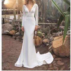 a woman in a white wedding dress standing on rocks with her handbag and looking off to the side