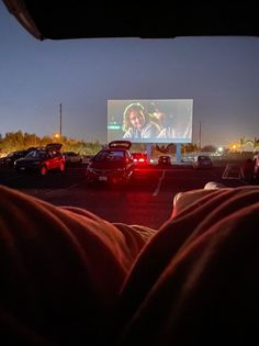 people watching a movie at night in a parking lot with cars parked on the side