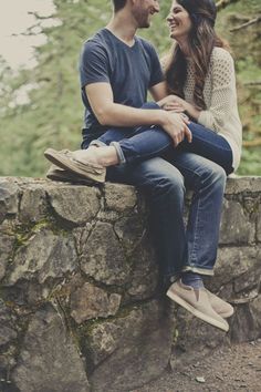 a man and woman sitting on top of a stone wall