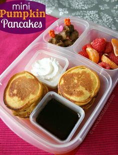 a plastic container filled with pancakes, fruit and sauces on top of a pink table cloth