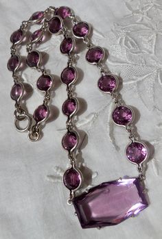 "This gorgeous Art Deco necklace is composed of faceted round crystals that are bezel-set in open-back settings. These sparkling stones are truly bezel-set, which are harder to find, not prong-set, as many sellers call prong-set crystals or glass that are unfoiled and in open-back settings. These are very sparkly, but they might be glass. They run all around the necklace. There is no chain. There is a larger, long hexagonal stone that is prong-set and is the centerpiece or pendant of the necklac Formal Round Faceted Crystal Necklaces, Faceted Crystal Necklaces For Formal Occasions, Formal Faceted Round Crystal Necklace, Formal Crystal Faceted Necklaces, Formal Faceted Crystal Necklaces, Formal Briolette Necklace With Bezel Setting, Gift Amethyst Bezel-set Jewelry, Elegant Faceted Purple Crystal Necklace, Purple Sterling Silver Crystal Pendant Necklace