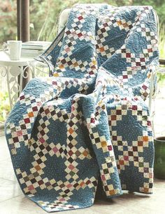 a chair with a quilt on it sitting in front of a window next to a potted plant