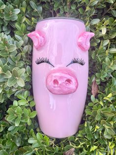 a pink vase with a pig's face on top of it surrounded by green leaves