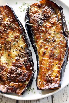 two grilled eggplant halves on a white plate with parmesan cheese