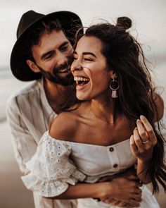 a man and woman are laughing together on the beach while one holds his arm around the other's shoulder