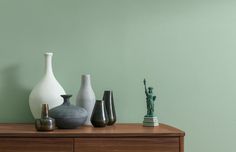 several vases are sitting on a dresser against a green wall with a statue in the corner