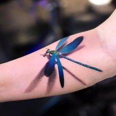 a blue dragonfly tattoo on the arm